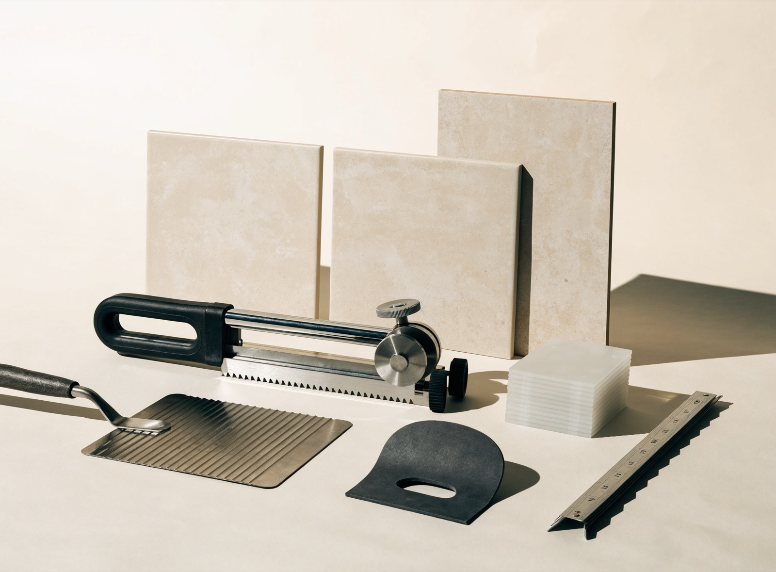 Materialaufnahme: Fliesenschneider, Zahnkelle, Fugenbrett, Fliesenkreuze und Großformatfliesen auf neutralem Studiogrund